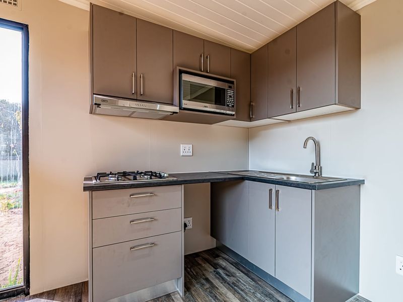 Compact modern kitchen featuring grey cabinetry, built-in gas hob, extractor fan, integrated microwave, and stainless steel sink with laminate flooring.