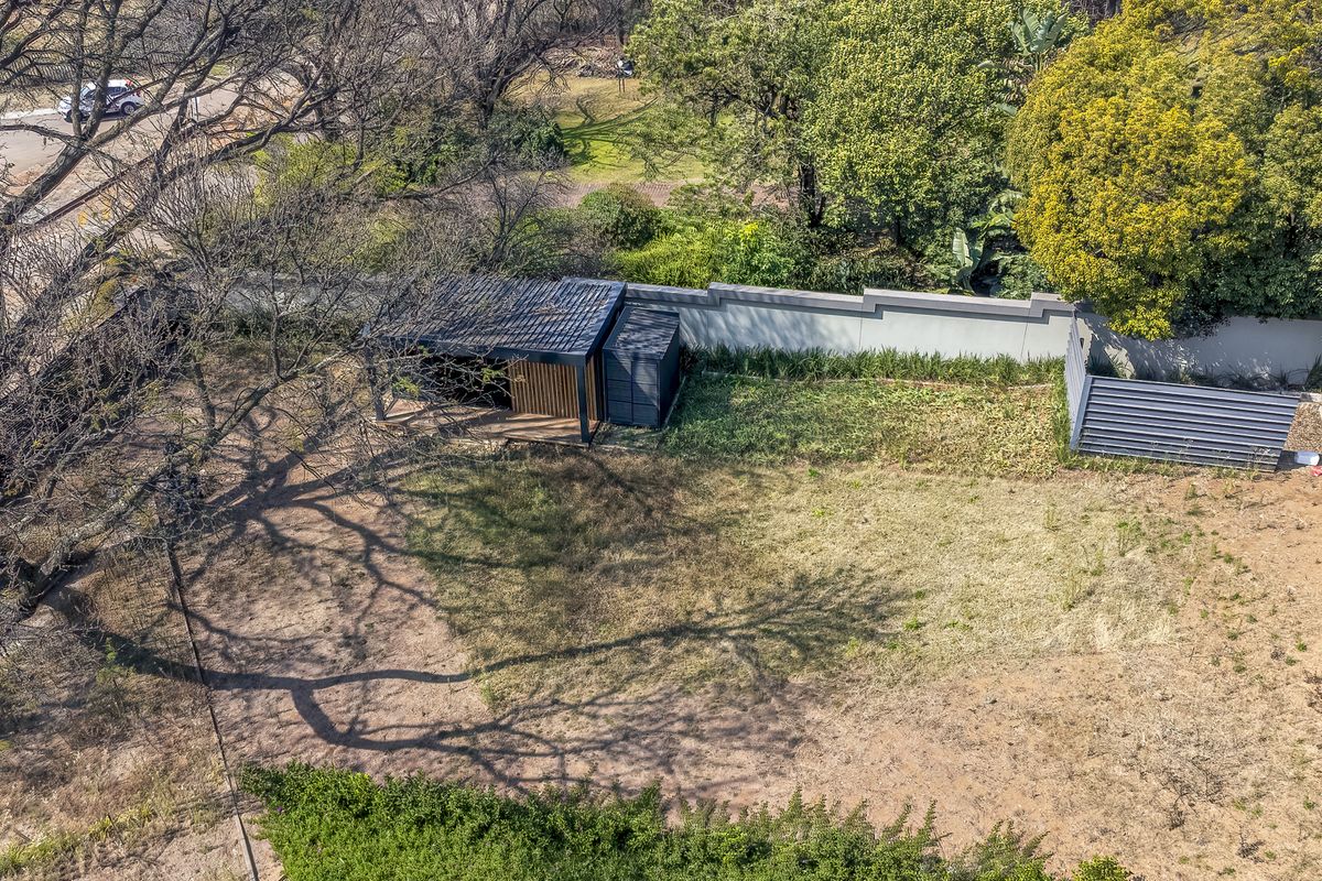 Aerial view of a vacant residential plot featuring a perimeter wall, mature trees, and a small existing structure.