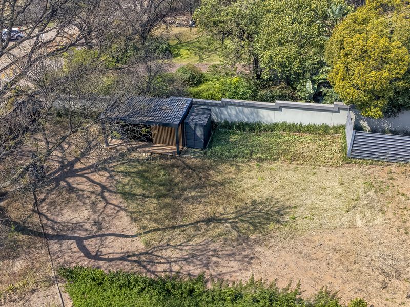 Aerial view of a vacant residential plot featuring a perimeter wall, mature trees, and a small existing structure.