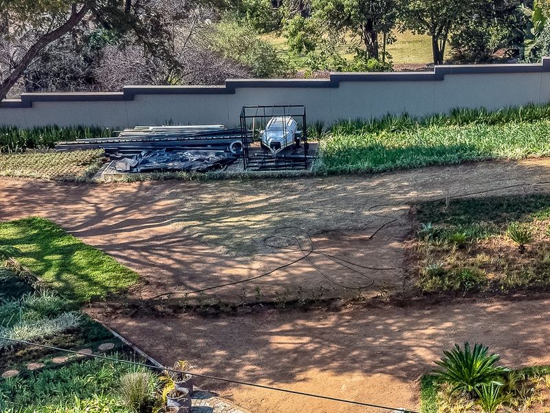 An elevated view of a residential garden area featuring established trees, landscaped garden beds, and a perimeter boundary wall.