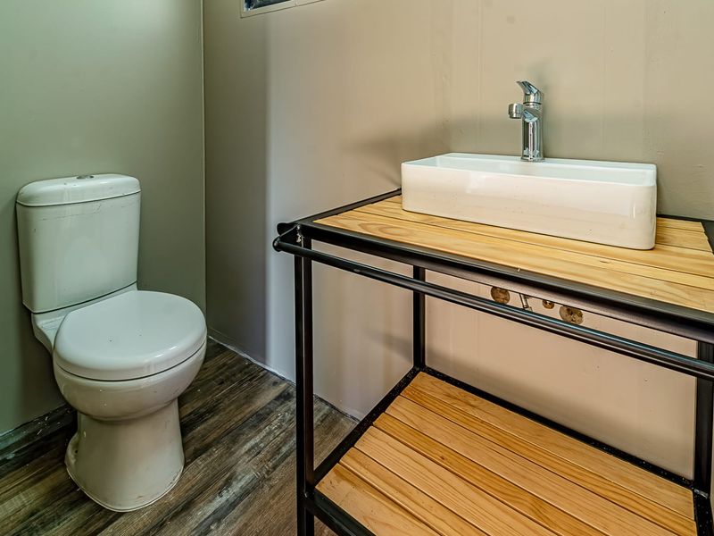 A modern bathroom featuring a white vessel sink on a metal and wood vanity frame, paired with a standard toilet and wood-look flooring.