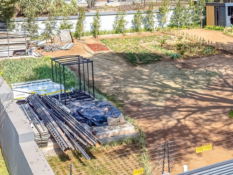 Aerial view of a residential vacant land plot featuring perimeter walls, electric fencing, and established garden areas with a small outbuilding.