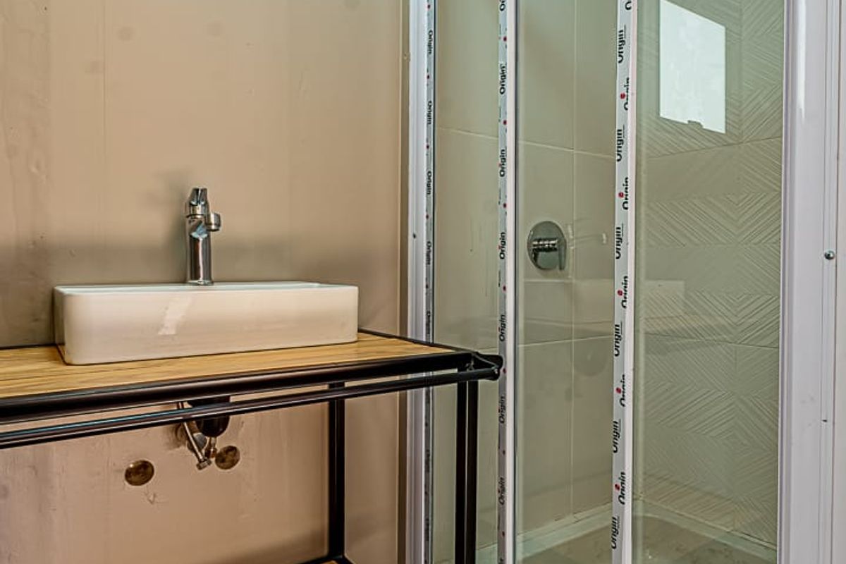 A compact bathroom featuring a modern vessel sink on a metal vanity frame and a glass-enclosed shower stall with tiled walls.