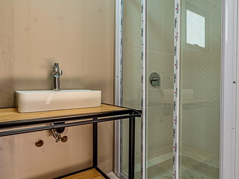A compact bathroom featuring a modern vessel sink on a metal vanity frame and a glass-enclosed shower stall with tiled walls.