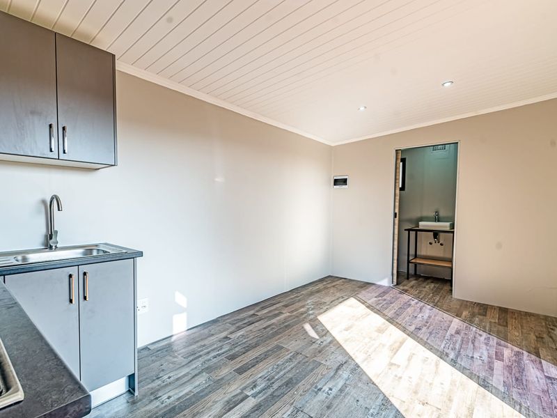 A clean, modern kitchen area featuring built-in cabinetry, a stainless steel sink, and wood-look laminate flooring, with an adjacent bathroom visible.