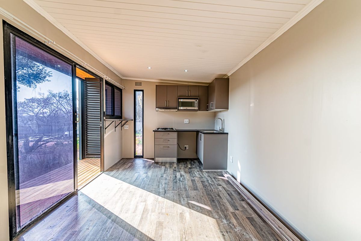 A compact, modern kitchen featuring built-in cabinetry, a gas cooktop, and integrated microwave, opening directly onto an outdoor deck through sliding glass doors.