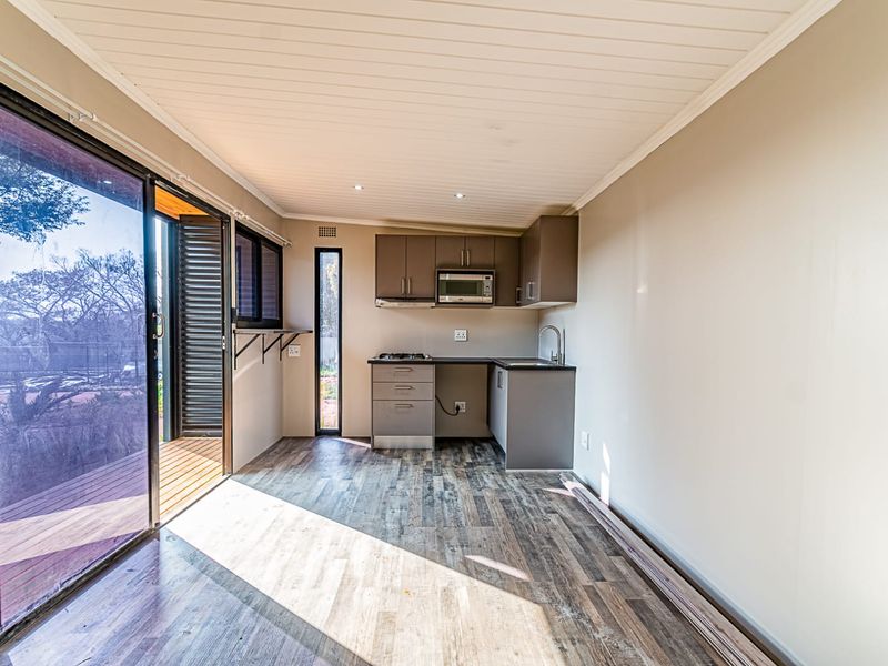 A compact, modern kitchen featuring built-in cabinetry, a gas cooktop, and integrated microwave, opening directly onto an outdoor deck through sliding glass doors.