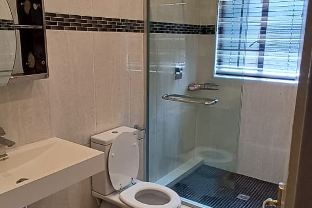 Modern bathroom featuring a walk-in glass shower, wall-mounted basin, and neutral tiled finishes with recessed lighting.