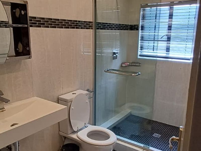Modern bathroom featuring a walk-in glass shower, wall-mounted basin, and neutral tiled finishes with recessed lighting.