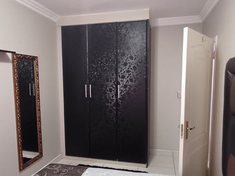 A bedroom featuring a dark patterned built-in wardrobe, tiled flooring, and crown molding detail.