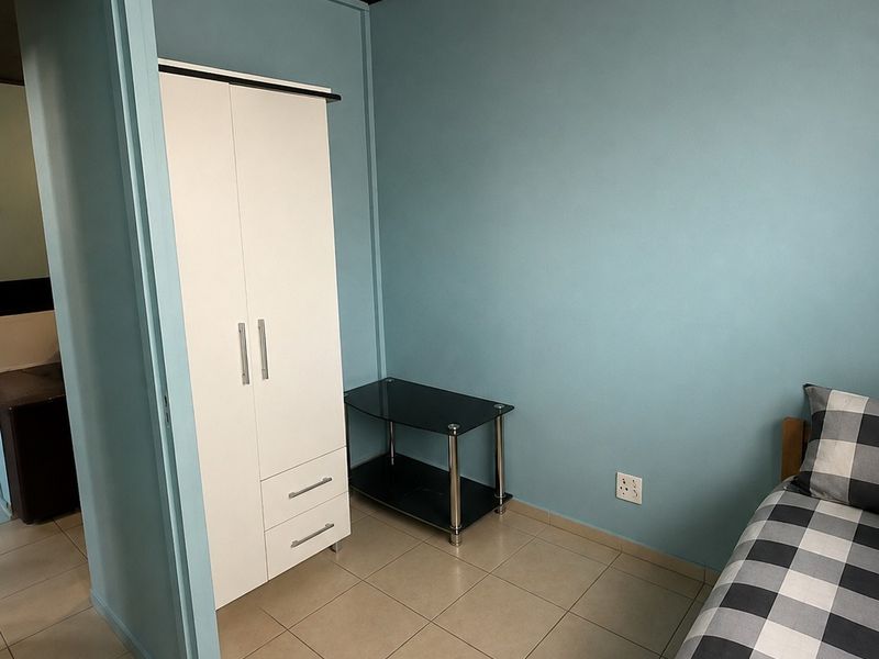 A bedroom featuring light blue walls, a dark ceiling, and tiled flooring, providing a functional space with basic lighting and electrical fixtures.