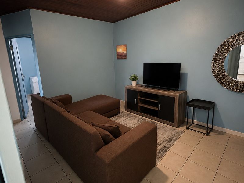 A living room featuring a distinctive timber-clad ceiling, neutral ceramic floor tiles, and light blue painted walls.
