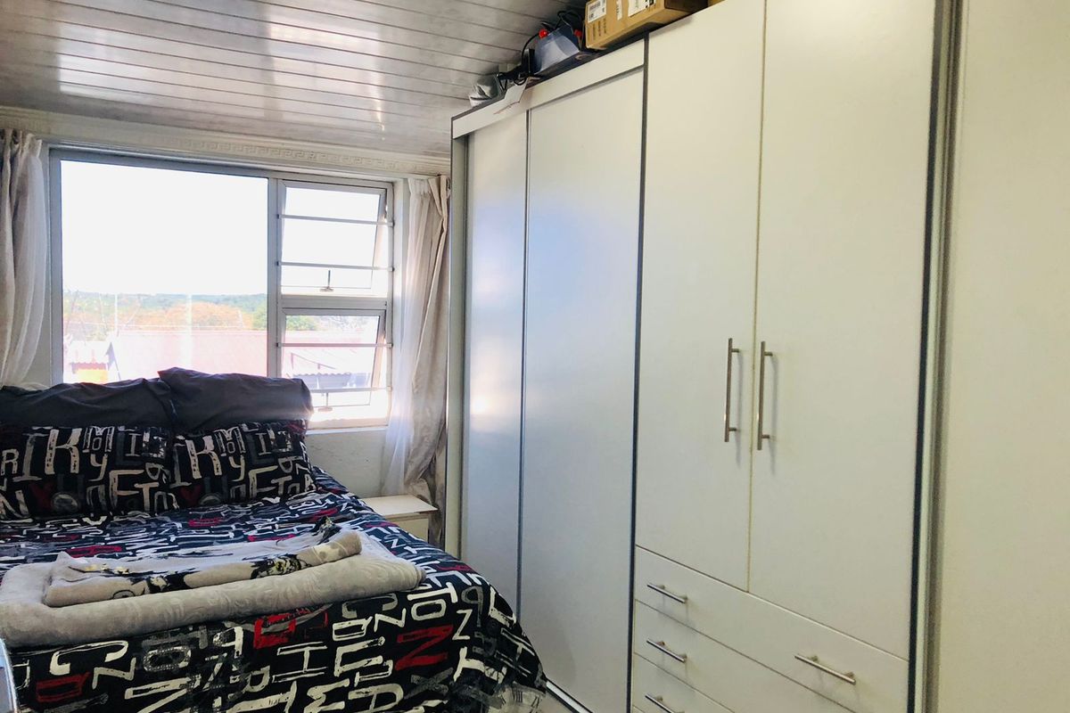 A bedroom featuring a large built-in wardrobe with sliding doors and drawers, complemented by a tongue and groove ceiling and natural light from the window.