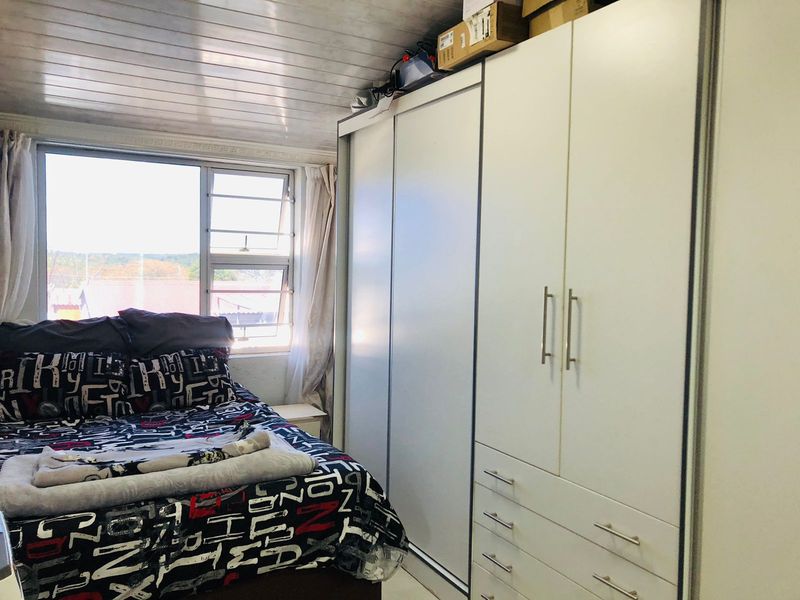A bedroom featuring a large built-in wardrobe with sliding doors and drawers, complemented by a tongue and groove ceiling and natural light from the window.