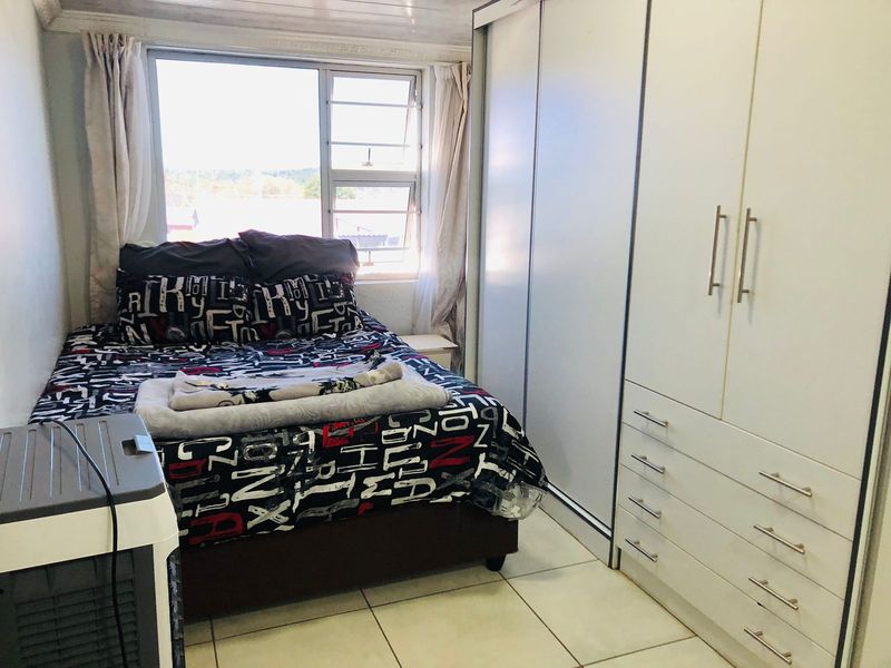 A functional bedroom featuring tiled flooring, a large built-in wardrobe with drawers, and a window providing natural light.