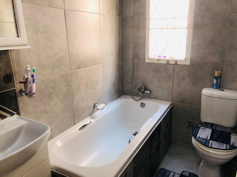 A functional bathroom featuring a bathtub with shower mixer, a standard toilet, and a basin, finished with neutral wall and floor tiles.