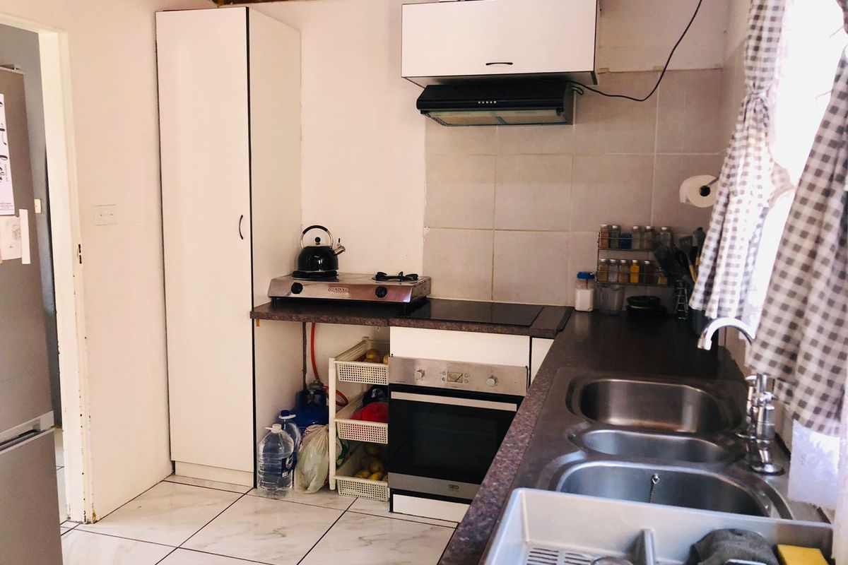 Compact kitchen featuring built-in oven, extractor fan, double sink, and tiled splashback, requiring some finishing work to the cabinetry and exposed utility areas.