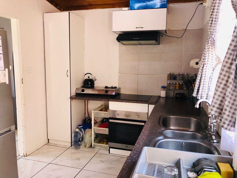 Compact kitchen featuring built-in oven, extractor fan, double sink, and tiled splashback, requiring some finishing work to the cabinetry and exposed utility areas.