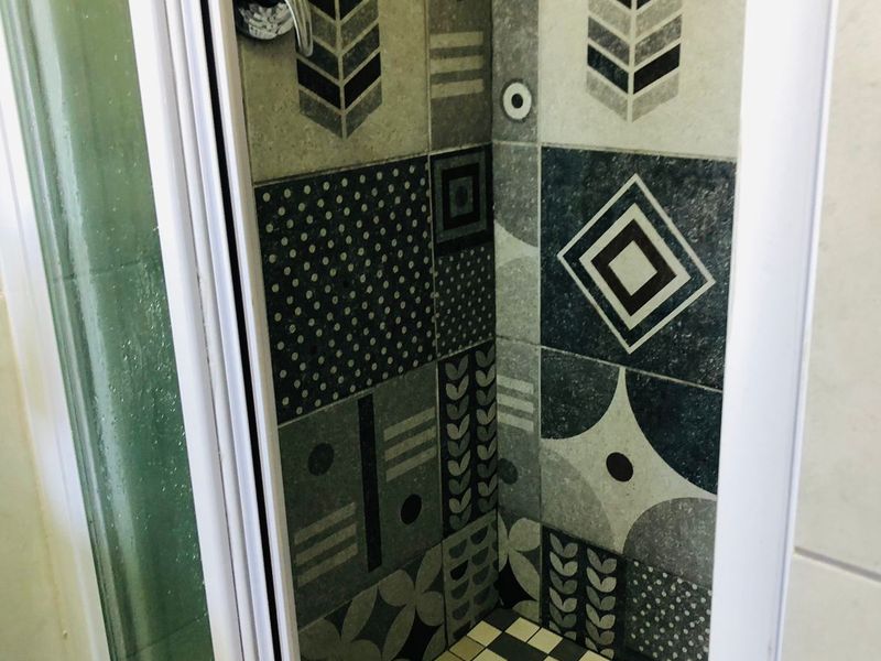 A compact shower stall featuring decorative patterned wall tiles and a classic checkered floor tile design.