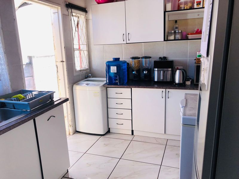 A functional laundry area featuring white built-in cabinetry, tiled flooring, and a tiled backsplash with direct access to the exterior.