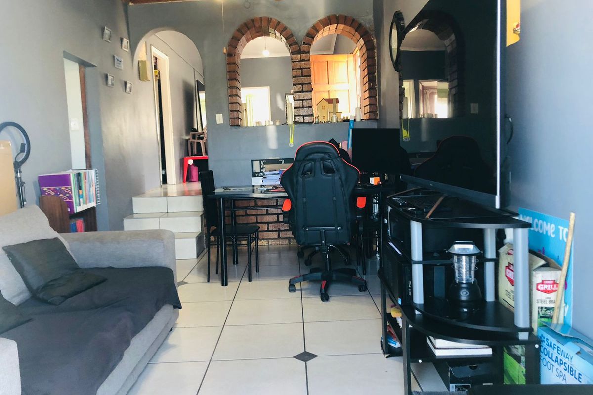 A living area featuring tiled flooring, distinctive brick archways, and a timber ceiling, offering a functional space with potential for cosmetic updates.