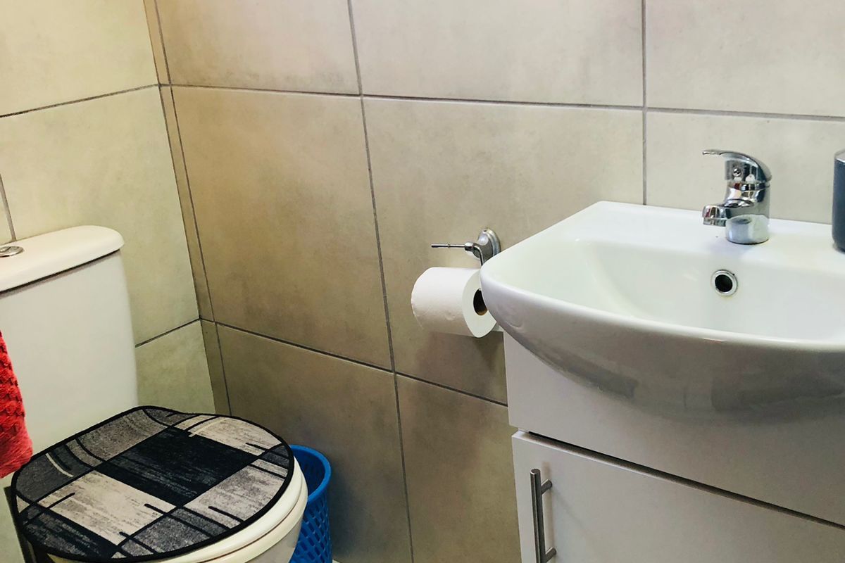 A compact bathroom featuring floor-to-ceiling wall tiles, a white vanity cabinet with integrated washbasin, and a standard toilet.