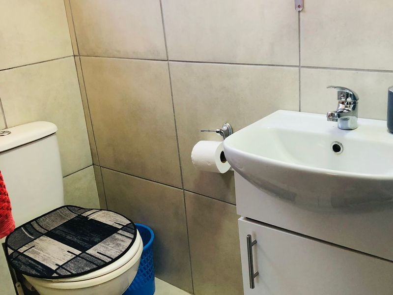 A compact bathroom featuring floor-to-ceiling wall tiles, a white vanity cabinet with integrated washbasin, and a standard toilet.