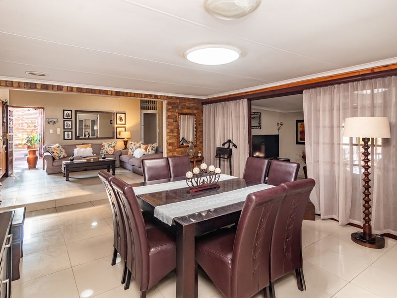 Spacious open-plan living and dining area featuring tiled floors, exposed brick accents, and seamless flow to the outdoor patio through sliding glass doors.