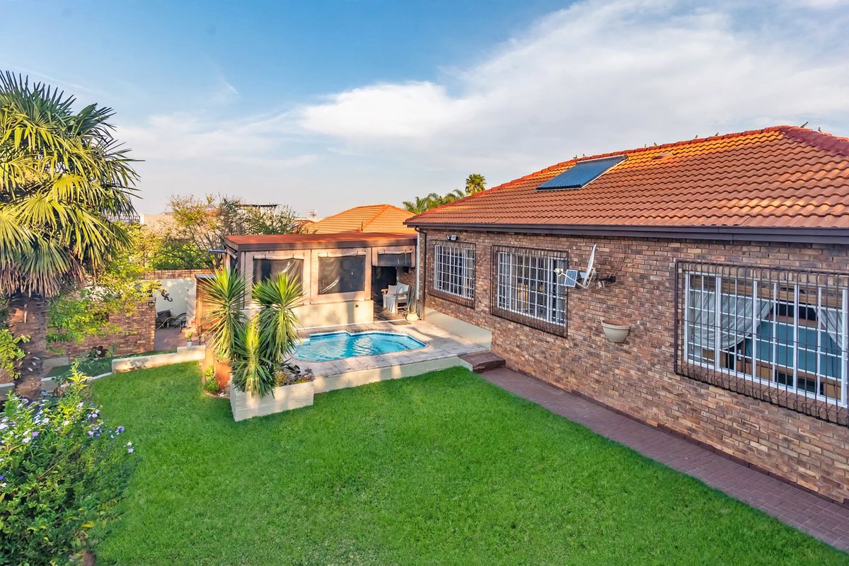 Rear view of a face brick cluster home featuring a private swimming pool, paved patio area, and a well-maintained garden with solar water heating.