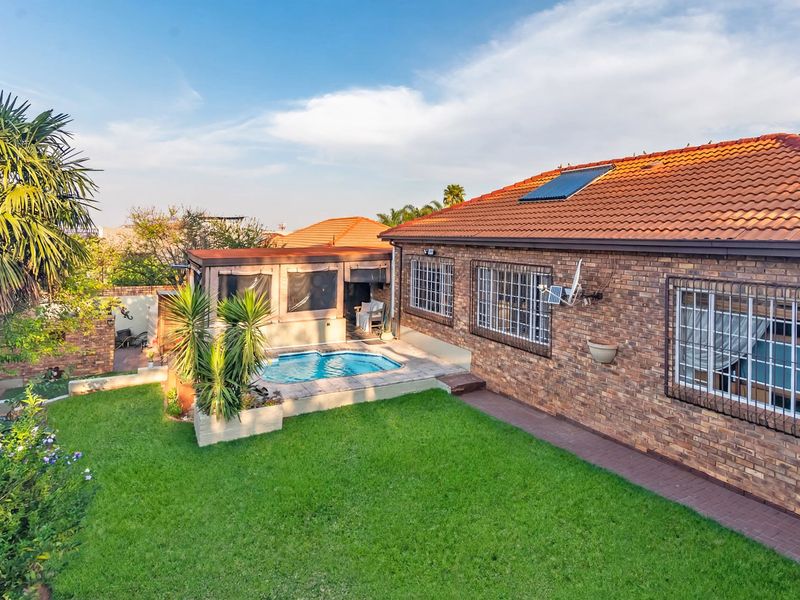 Rear view of a face brick cluster home featuring a private swimming pool, paved patio area, and a well-maintained garden with solar water heating.