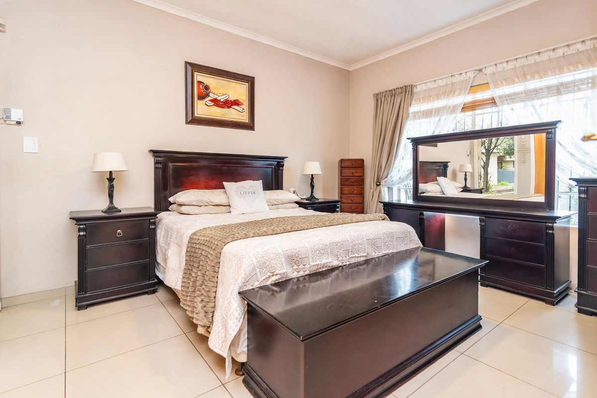A well-maintained bedroom featuring neutral wall tones, tiled flooring, and a large window allowing for natural light.