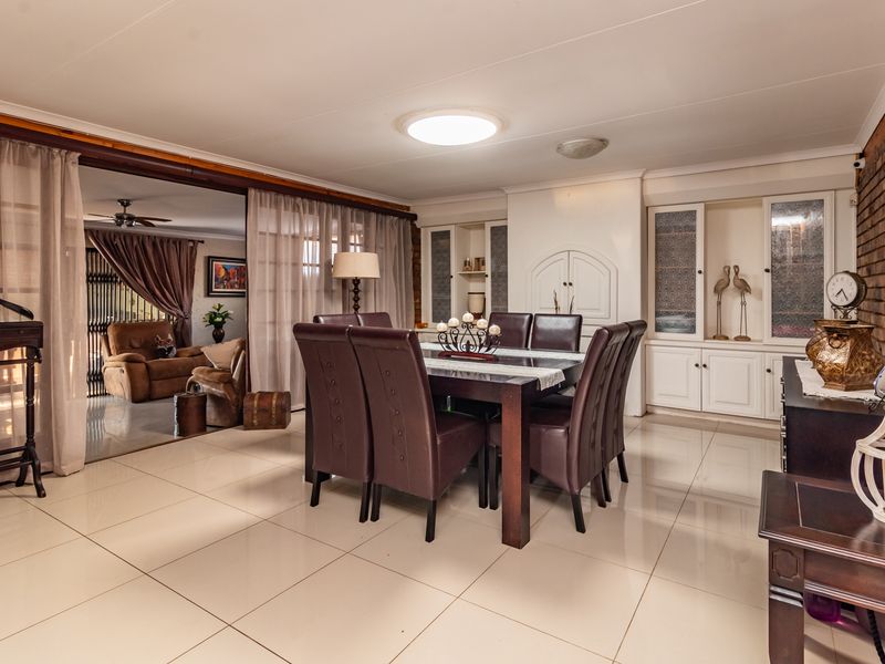 Spacious dining room featuring polished tile flooring, built-in display cabinetry, and an exposed brick feature wall, with sliding doors leading to an adjacent living area.