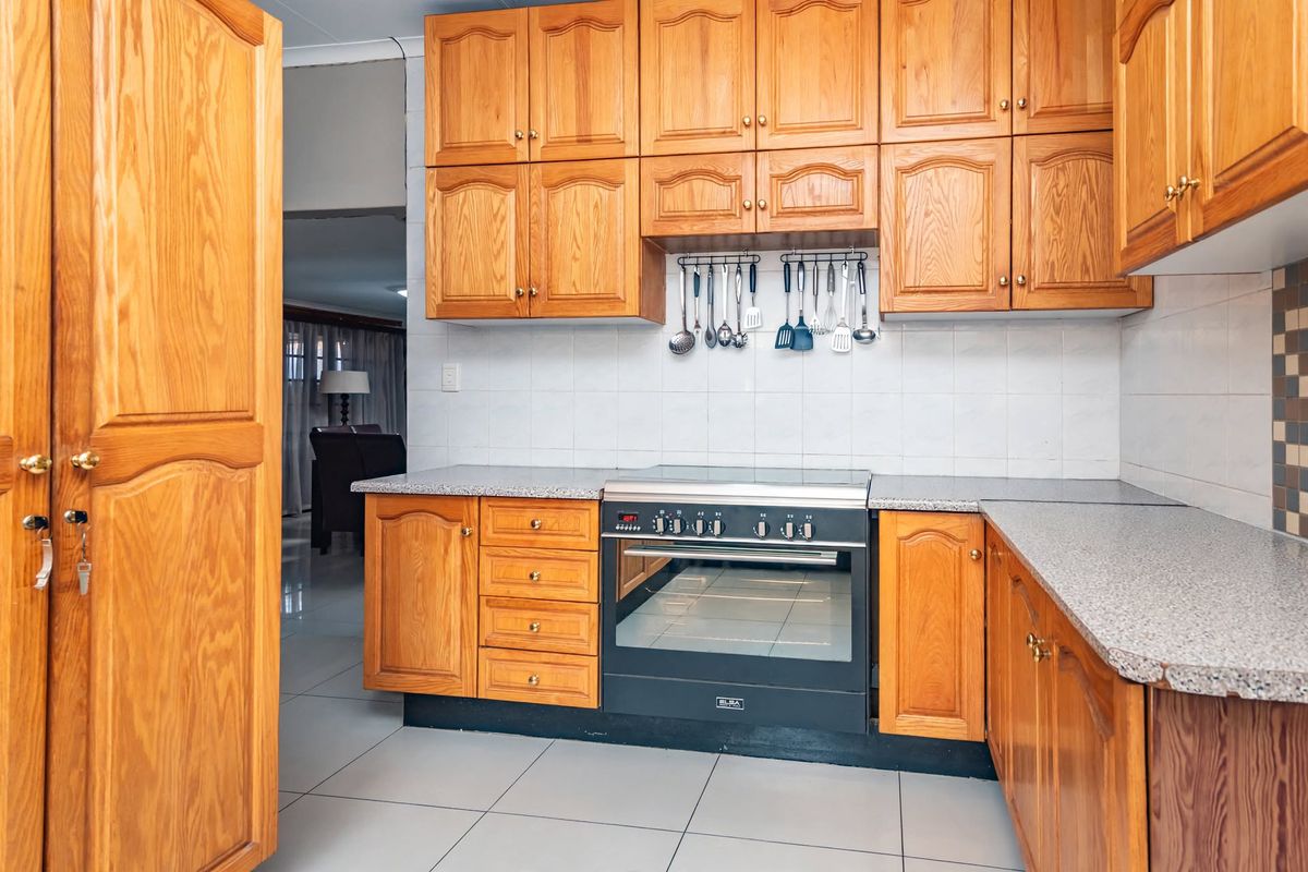 A functional kitchen featuring warm-toned wooden cabinetry, granite countertops, a built-in oven with a ceramic hob, and neutral tiled flooring.
