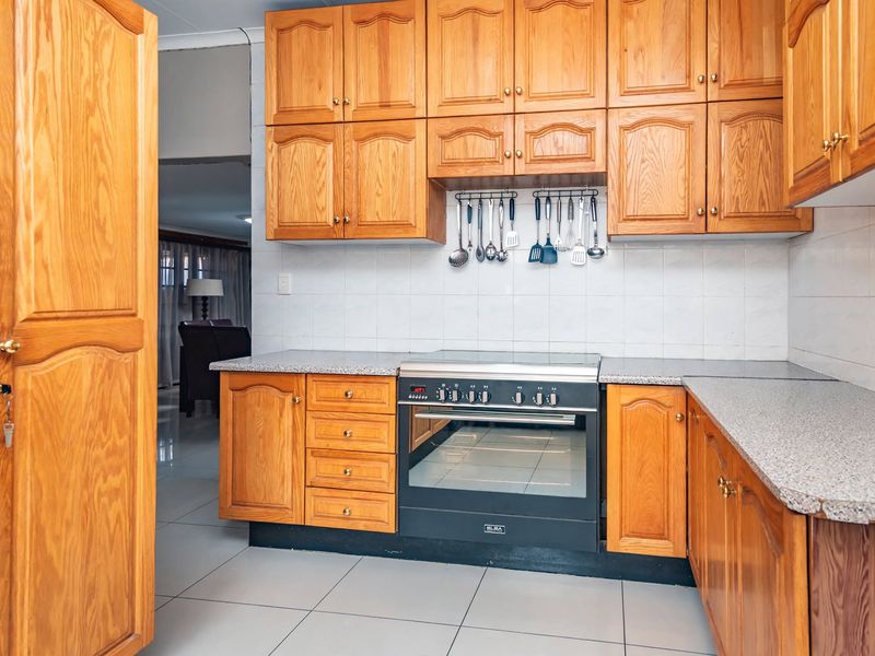 A functional kitchen featuring warm-toned wooden cabinetry, granite countertops, a built-in oven with a ceramic hob, and neutral tiled flooring.