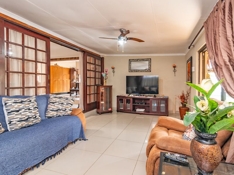 A comfortable living room featuring tiled flooring, a ceiling fan, and large sliding wooden doors that connect to the adjacent living space.