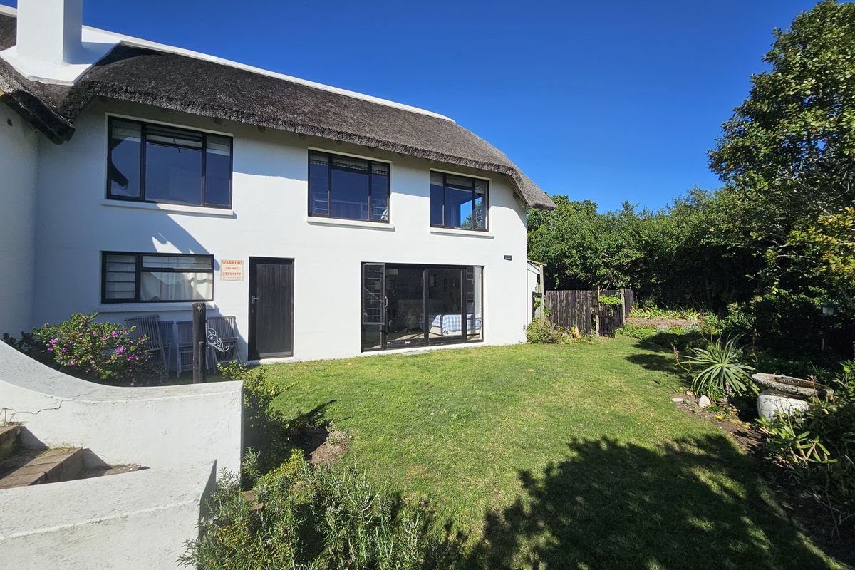 Rear view of a white-walled house featuring a traditional thatched roof, large sliding glass doors, and a well-maintained garden lawn.