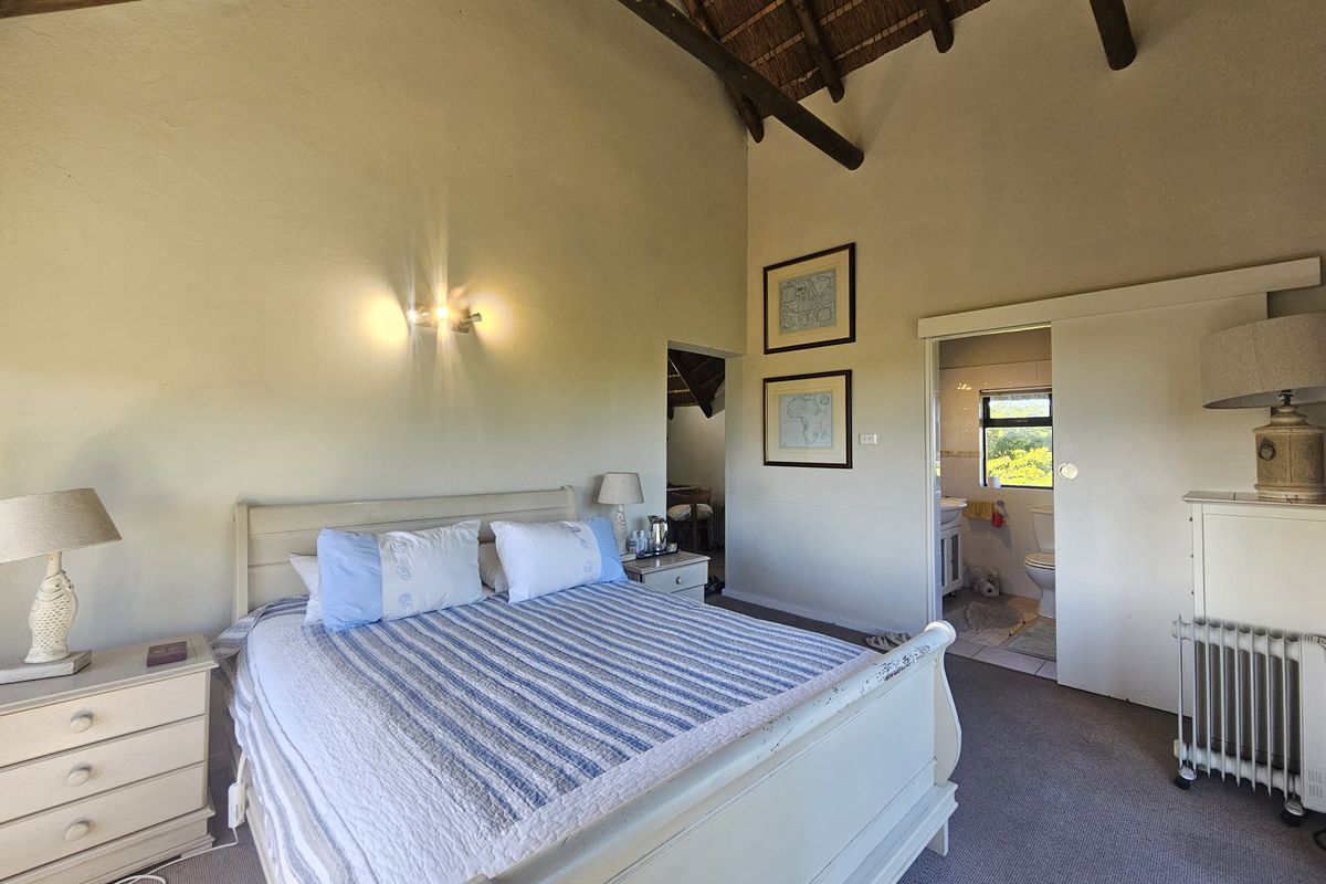 A bedroom featuring a high vaulted thatched ceiling with exposed timber rafters and an adjoining en-suite bathroom accessed via a sliding door.