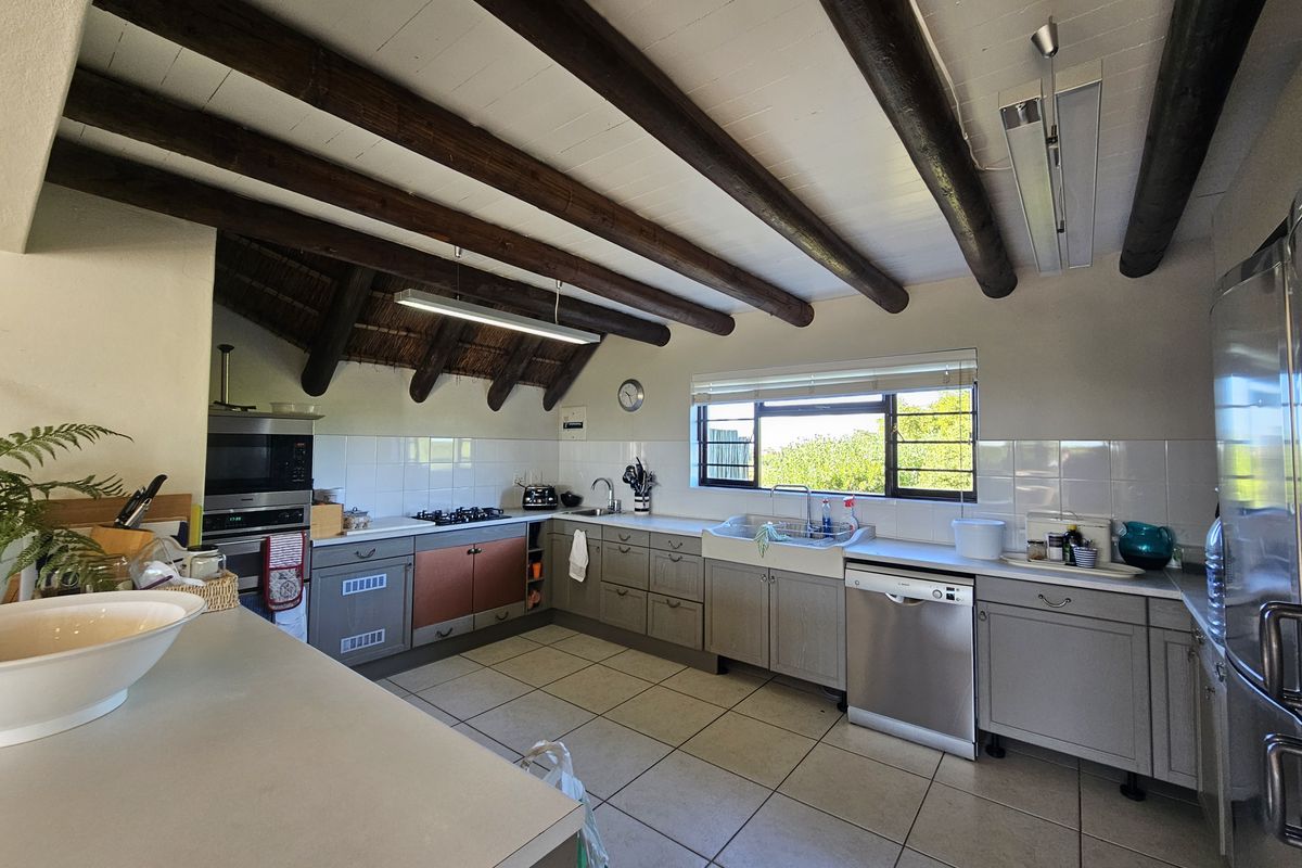 Spacious kitchen featuring exposed timber ceiling beams, tiled flooring, a farmhouse sink, and built-in cabinetry with integrated appliances.