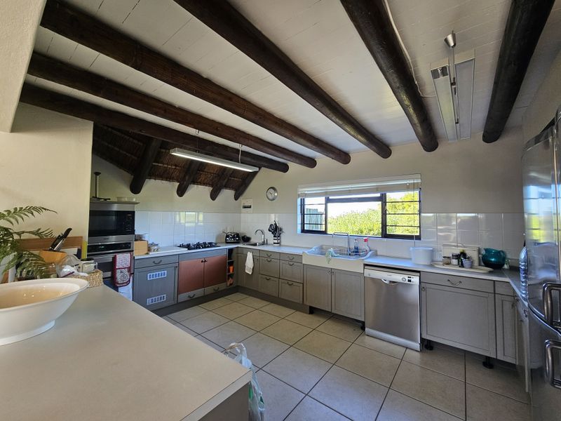 Spacious kitchen featuring exposed timber ceiling beams, tiled flooring, a farmhouse sink, and built-in cabinetry with integrated appliances.