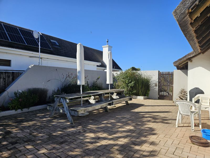 A paved outdoor patio area featuring a boundary wall, timber gate, and access to the main dwelling with a thatched roof section.