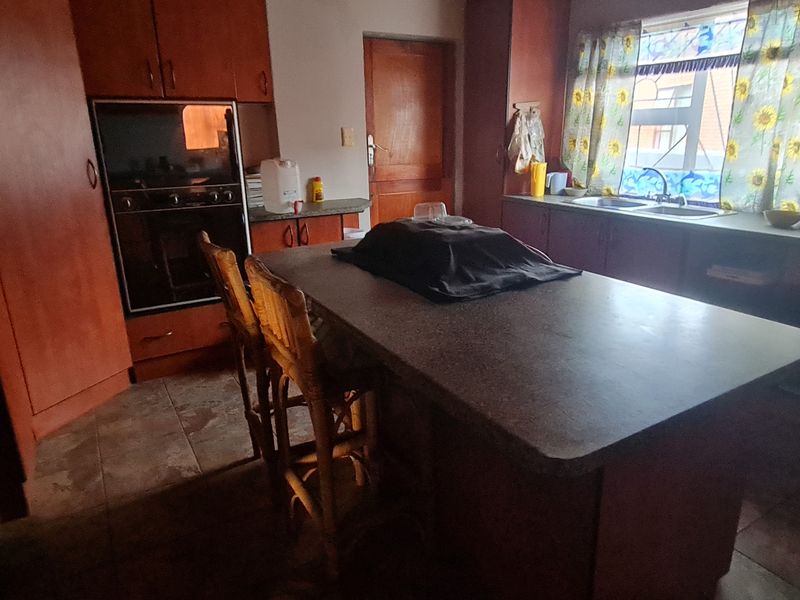 A dated kitchen featuring wooden cabinetry, a central island, built-in oven, and double basin sink with tiled flooring.