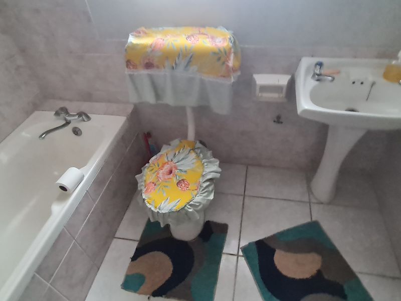 A dated bathroom featuring a bathtub, pedestal basin, and toilet with tiled finishes. The space requires maintenance due to visible wall mold.