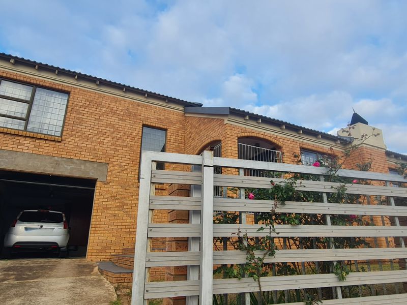 Front elevation of a double-story face brick house featuring a double garage, concrete driveway, and a modern slatted boundary fence.