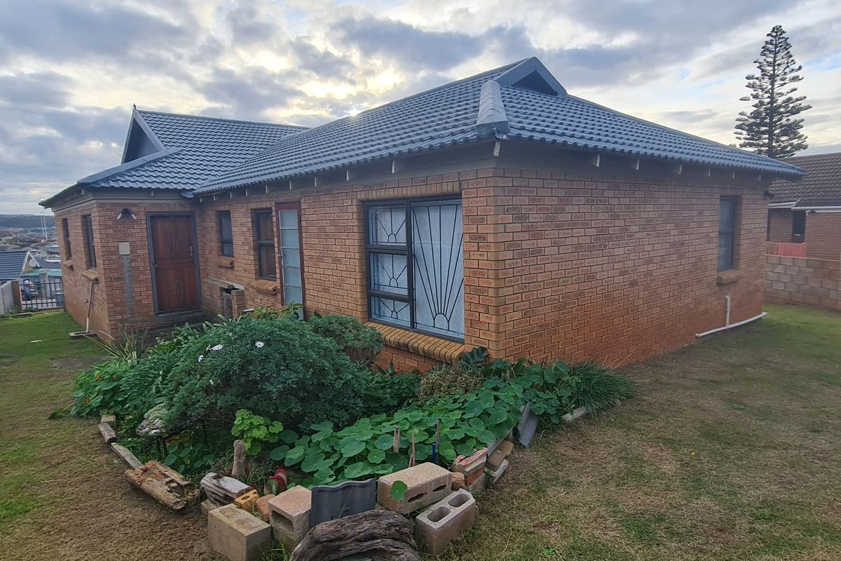 Rear view of a face-brick house featuring a tiled roof, security bars on windows, and a surrounding garden area with boundary walling.