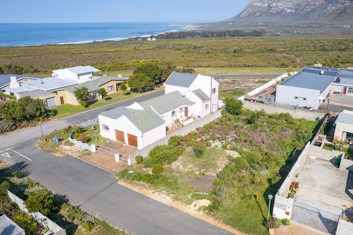 Aerial view of a residential property featuring a pitched roof house, double garage, and surrounding coastal landscape.