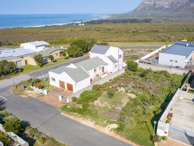 Aerial view of a residential property featuring a pitched roof house, double garage, and surrounding coastal landscape.