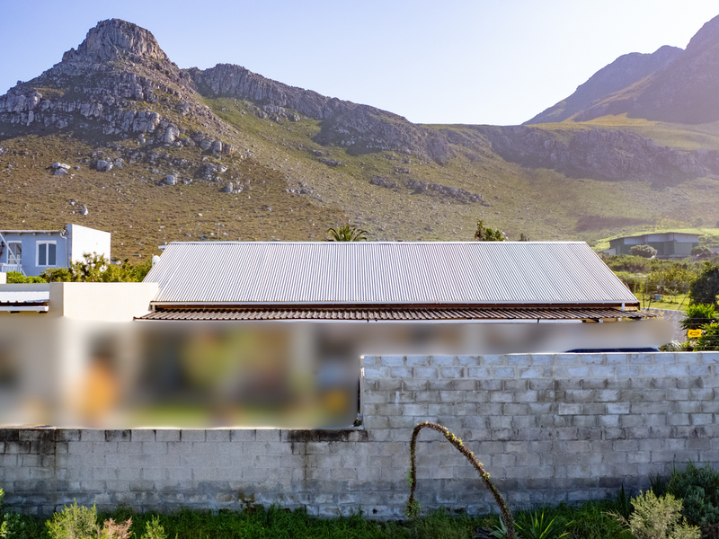 Rear view of the property featuring a corrugated metal roof and a concrete block boundary wall with mountain views in the background.