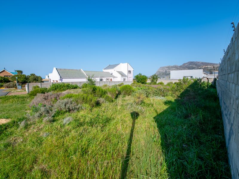 A vacant residential plot featuring a perimeter wall with electric fencing, surrounded by established neighborhood properties and mountain views.