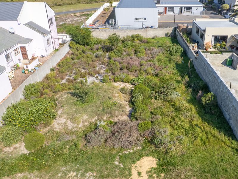 An aerial view of a vacant residential plot enclosed by boundary walls, featuring natural vegetation and surrounding residential properties.