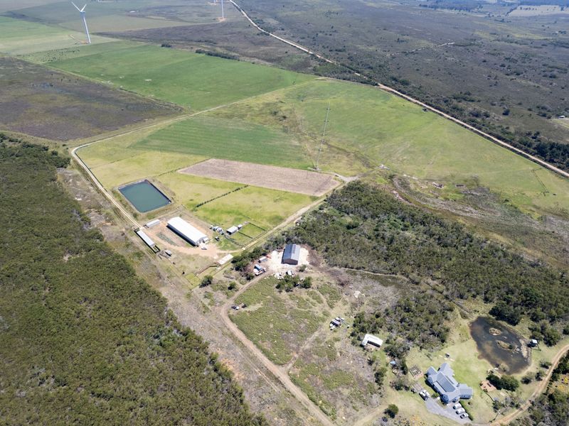 Aerial view of a large residential land parcel featuring a main residence, multiple outbuildings, a farm dam, and extensive open grazing or agricultural land.